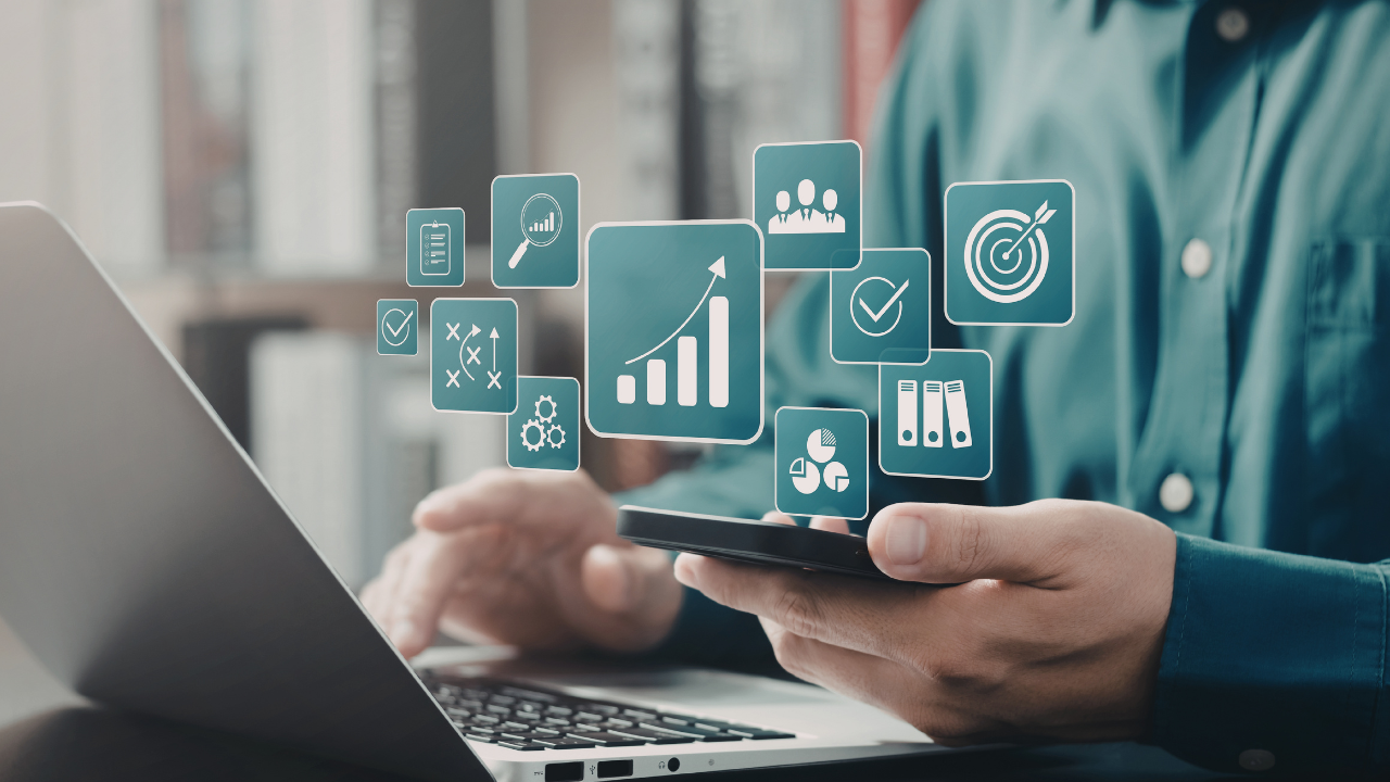 Businessperson using a smartphone and laptop with floating analytics icons (charts, graphs, and dashboards) representing data-driven insights and analytics access.